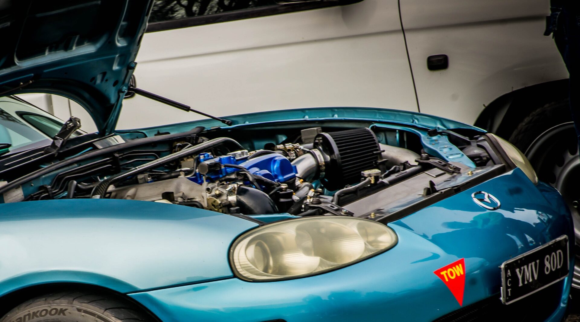 Blue Mazda sports car with its hood open exposing the engine bay and a black air filter.
