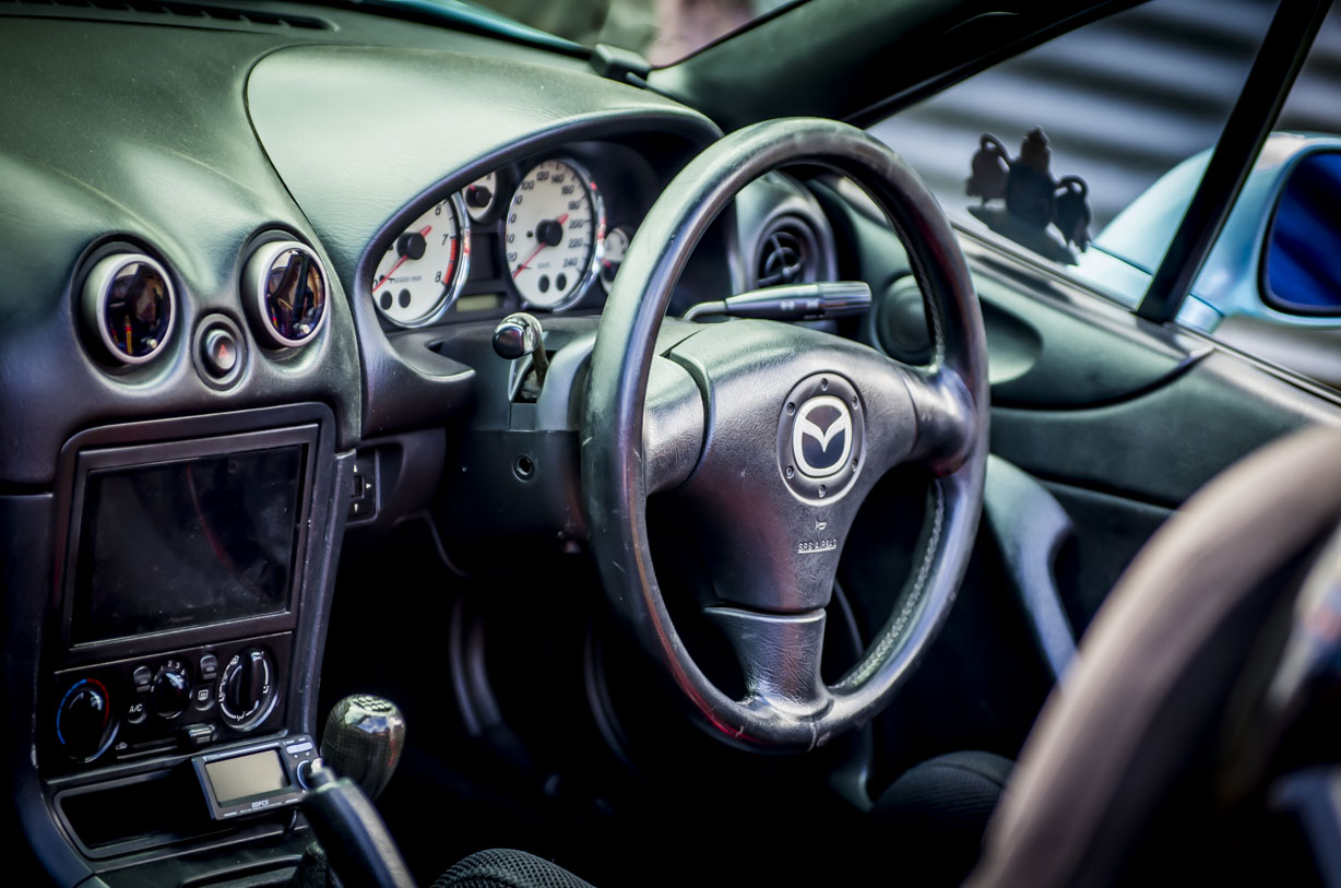 Close-up of a right-hand drive Mazda car interior focusing on the steering wheel and dashboard.