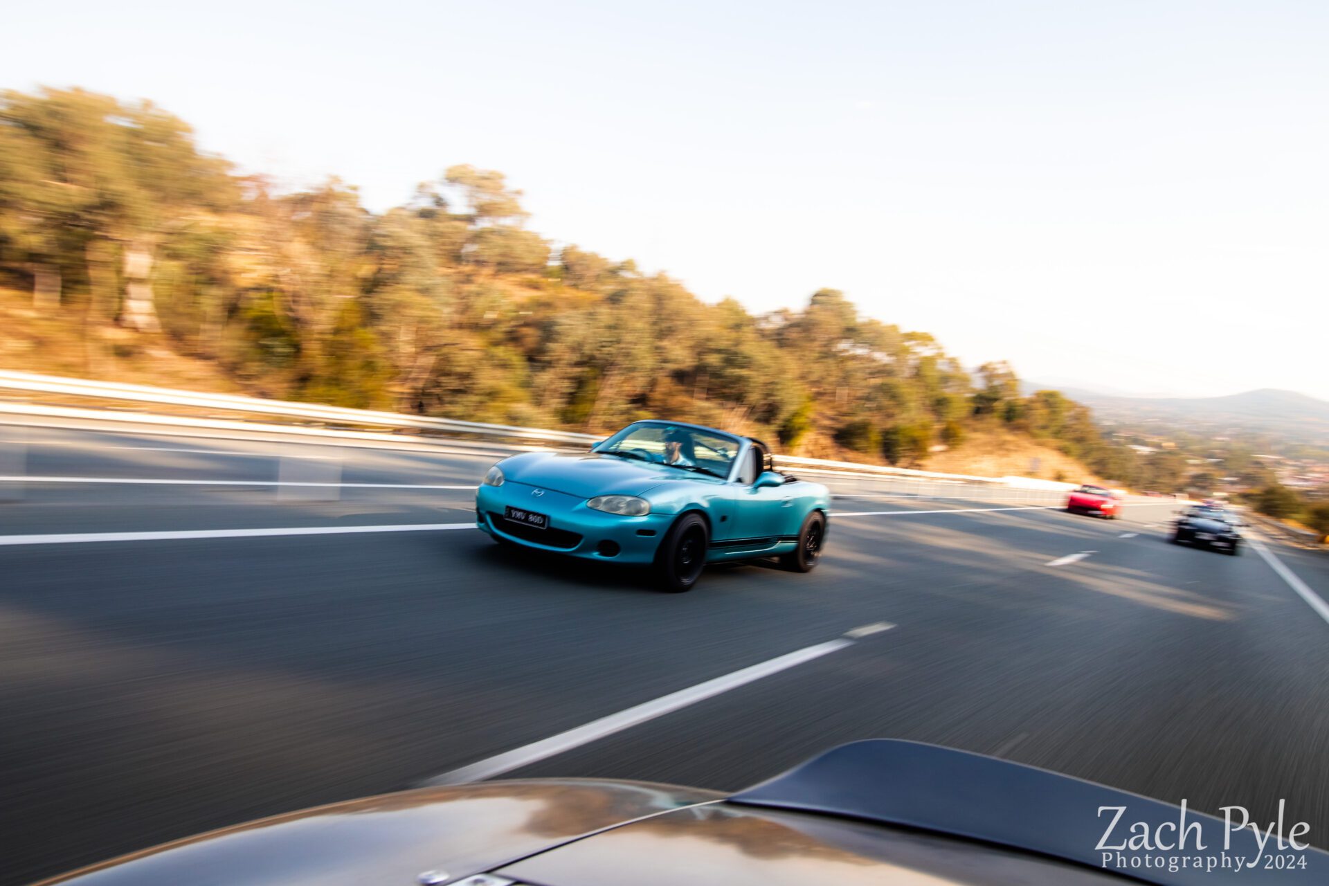 Blue convertible sports car driving fast on a highway with blurred background and other cars.
