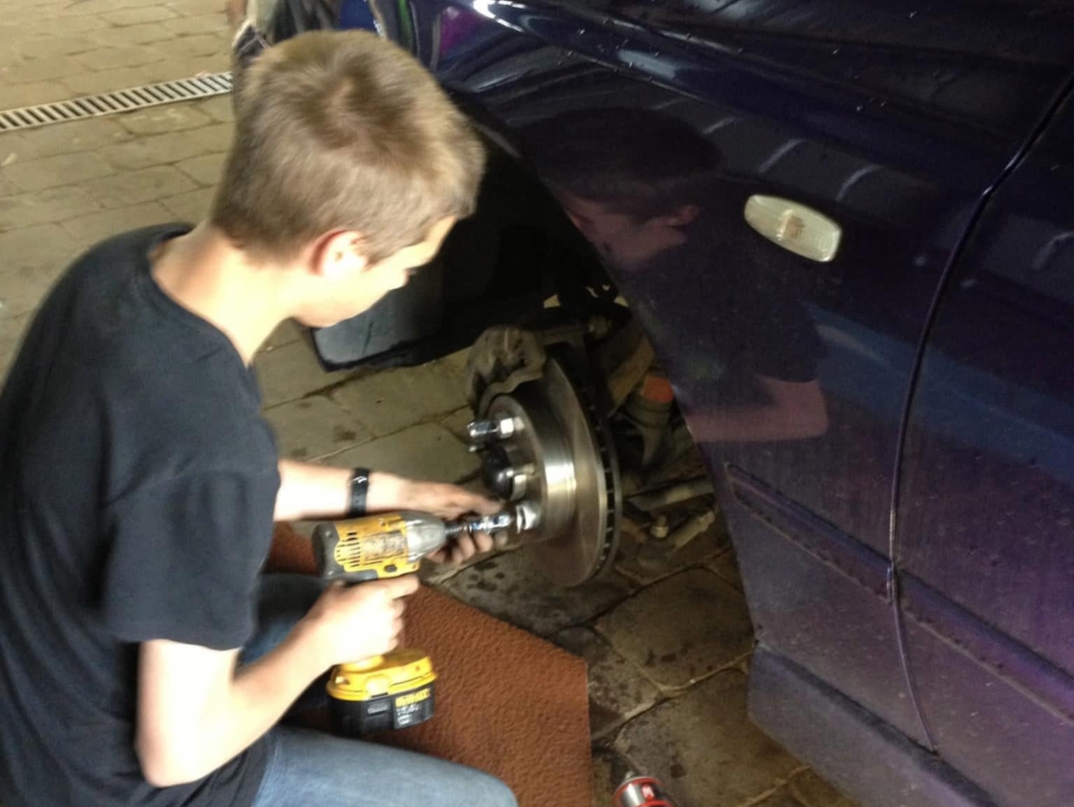 Person using a power tool to work on a car brake rotor in a garage setting.