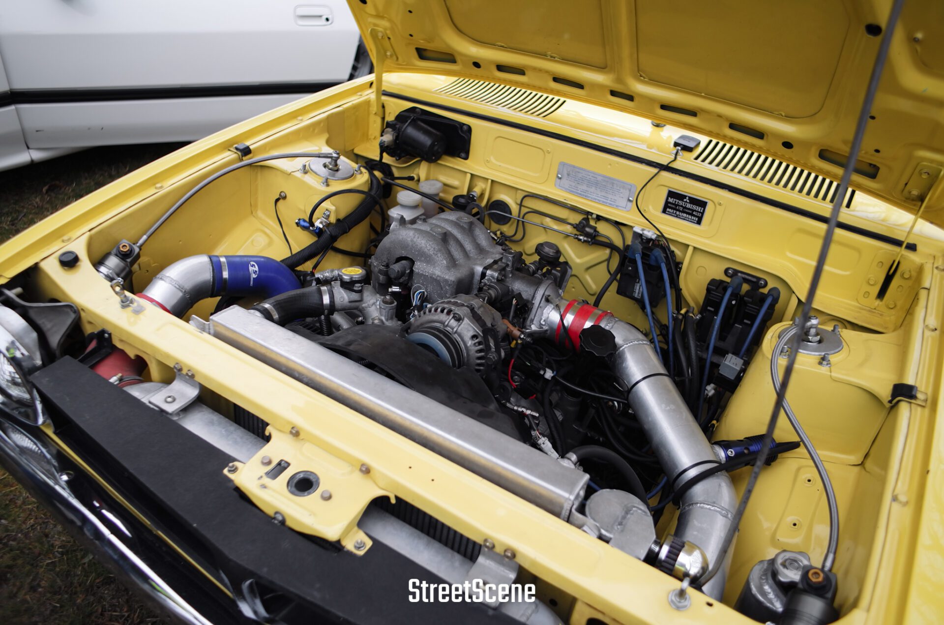 Yellow vintage car engine bay showing a detailed turbocharged engine setup and components.