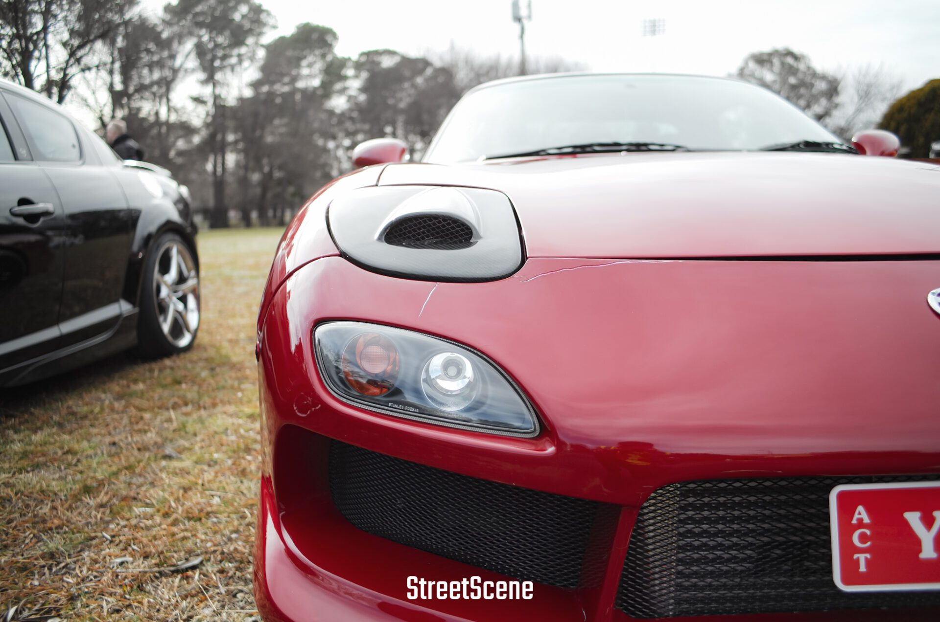 Close-up of a red sports car front headlight and hood with a black car parked beside it.