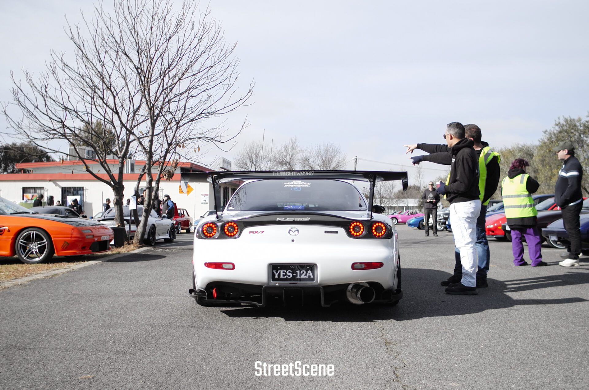 Rear view of a white Mazda RX-7 with a large spoiler at a car meet.