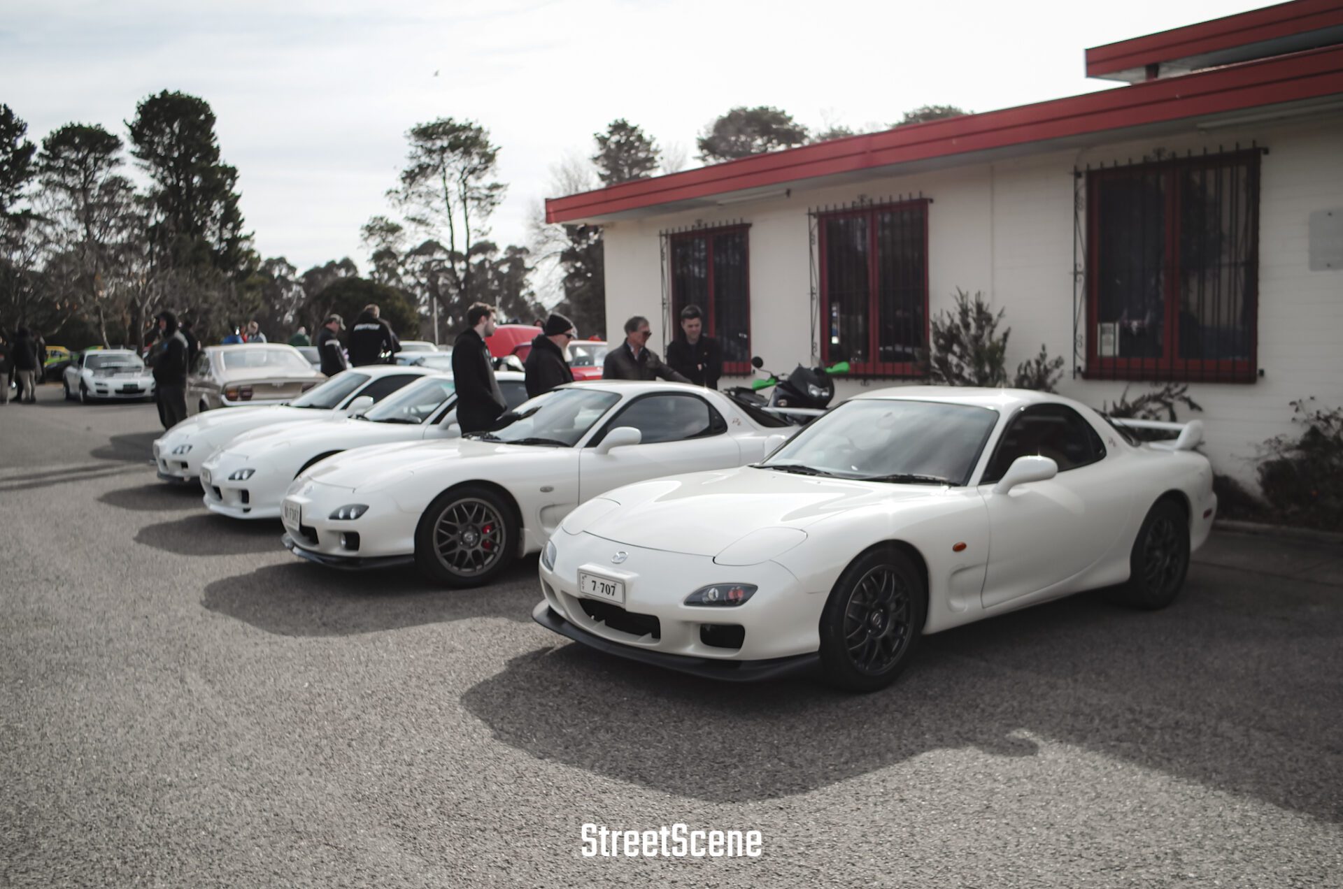 Row of white sports cars parked outside a building with people standing nearby.