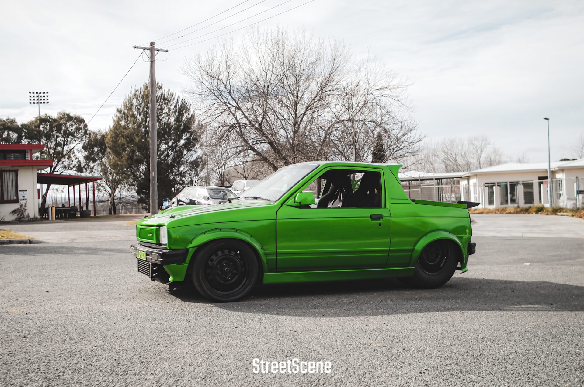 Bright green modified compact car parked on a street with bare trees and buildings in background.