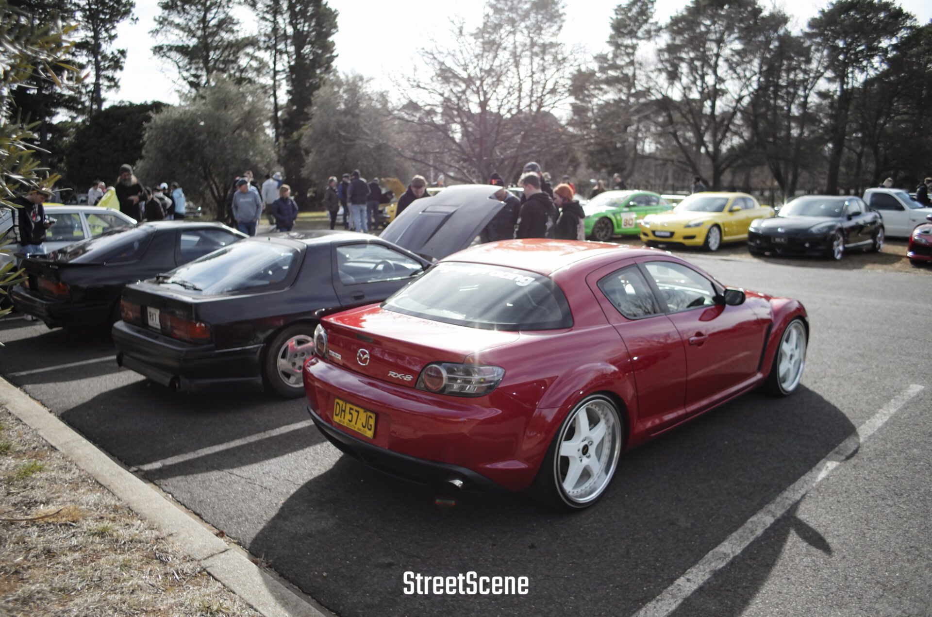 Red Mazda RX-8 and black sports cars parked at an outdoor car meet with people in the background.