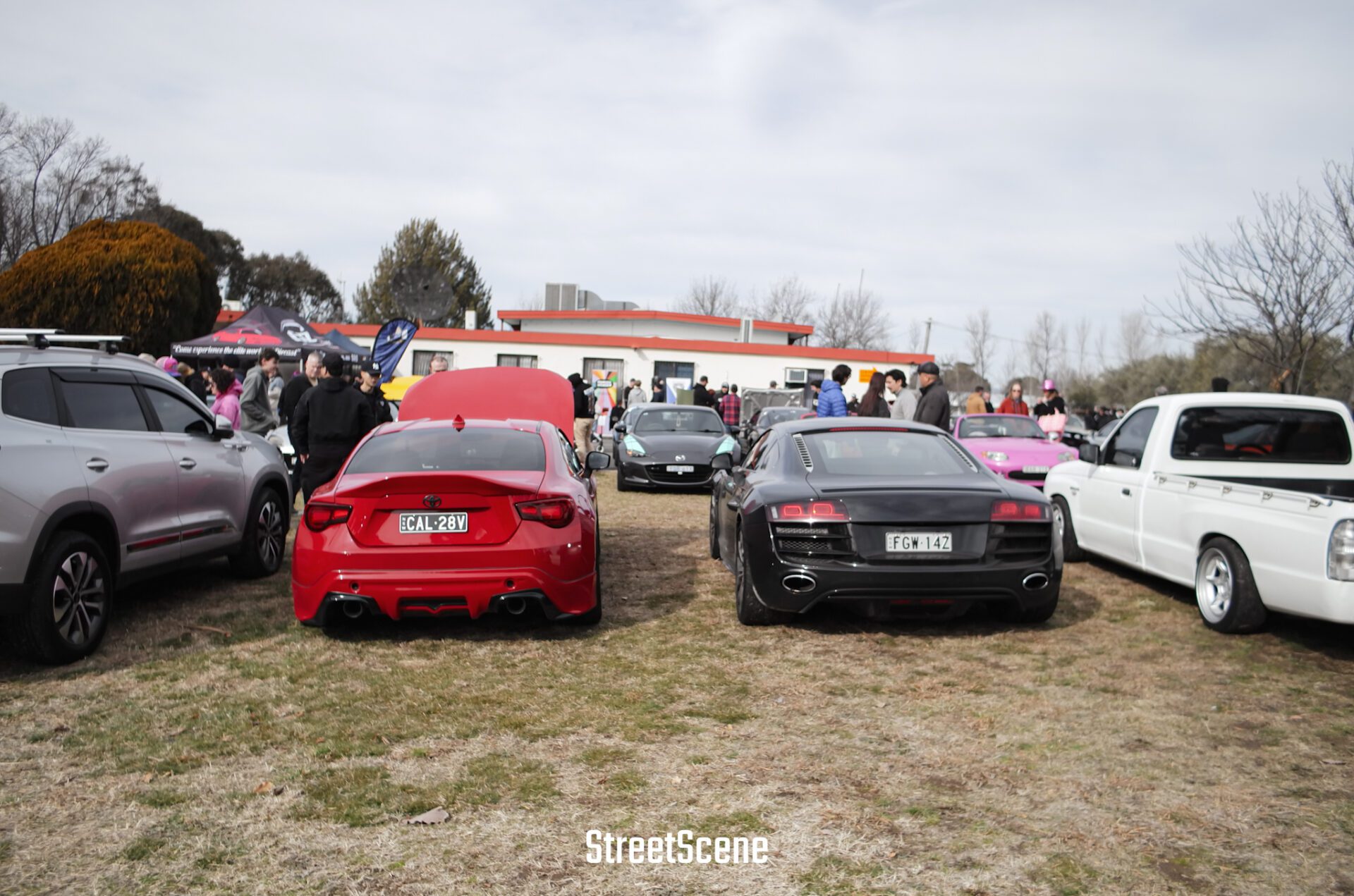 Cars parked on grass with people gathered around at an outdoor car show event.