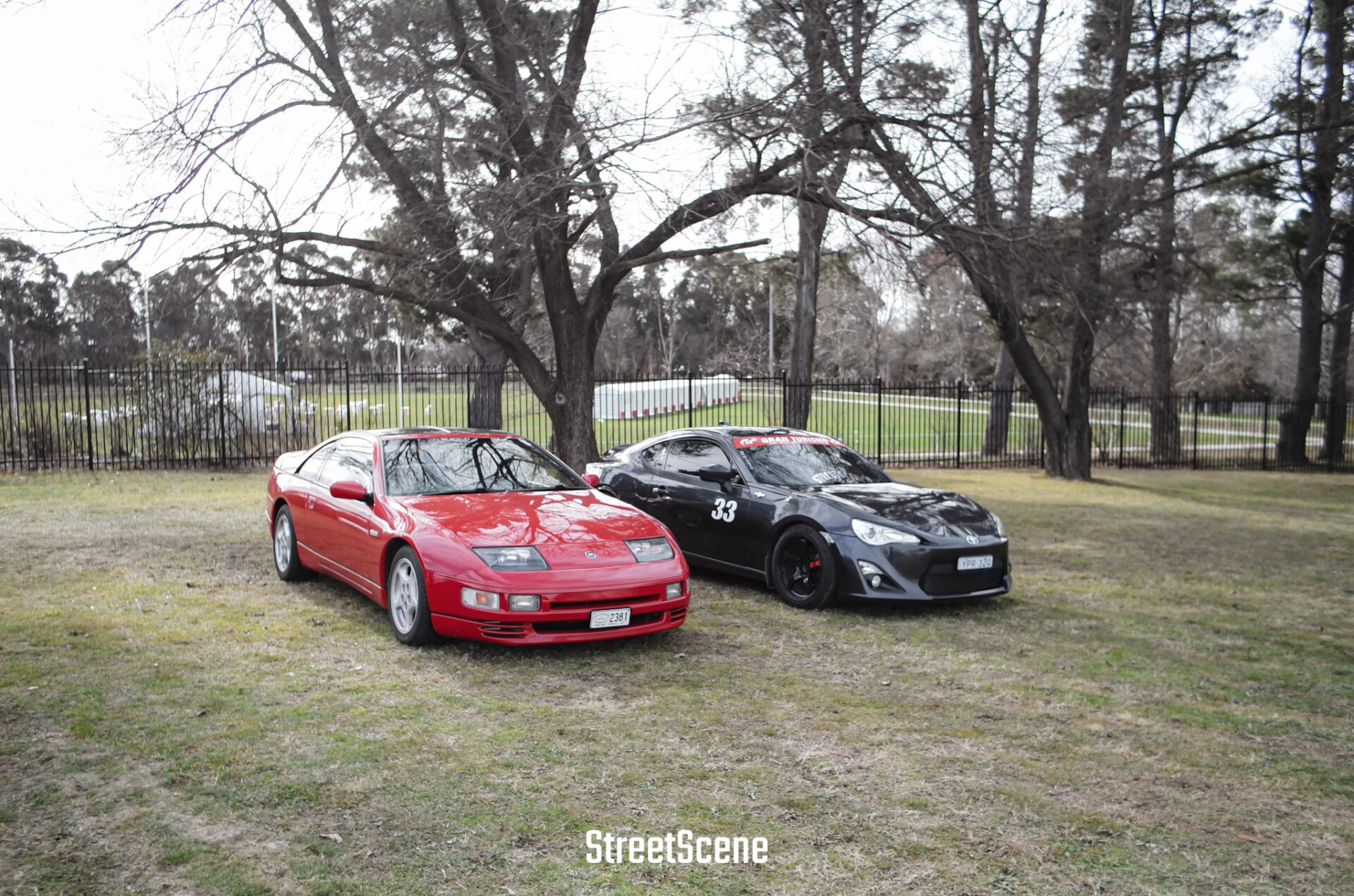 Two sports cars, one red and one black with number 33, parked on grass by a tree.